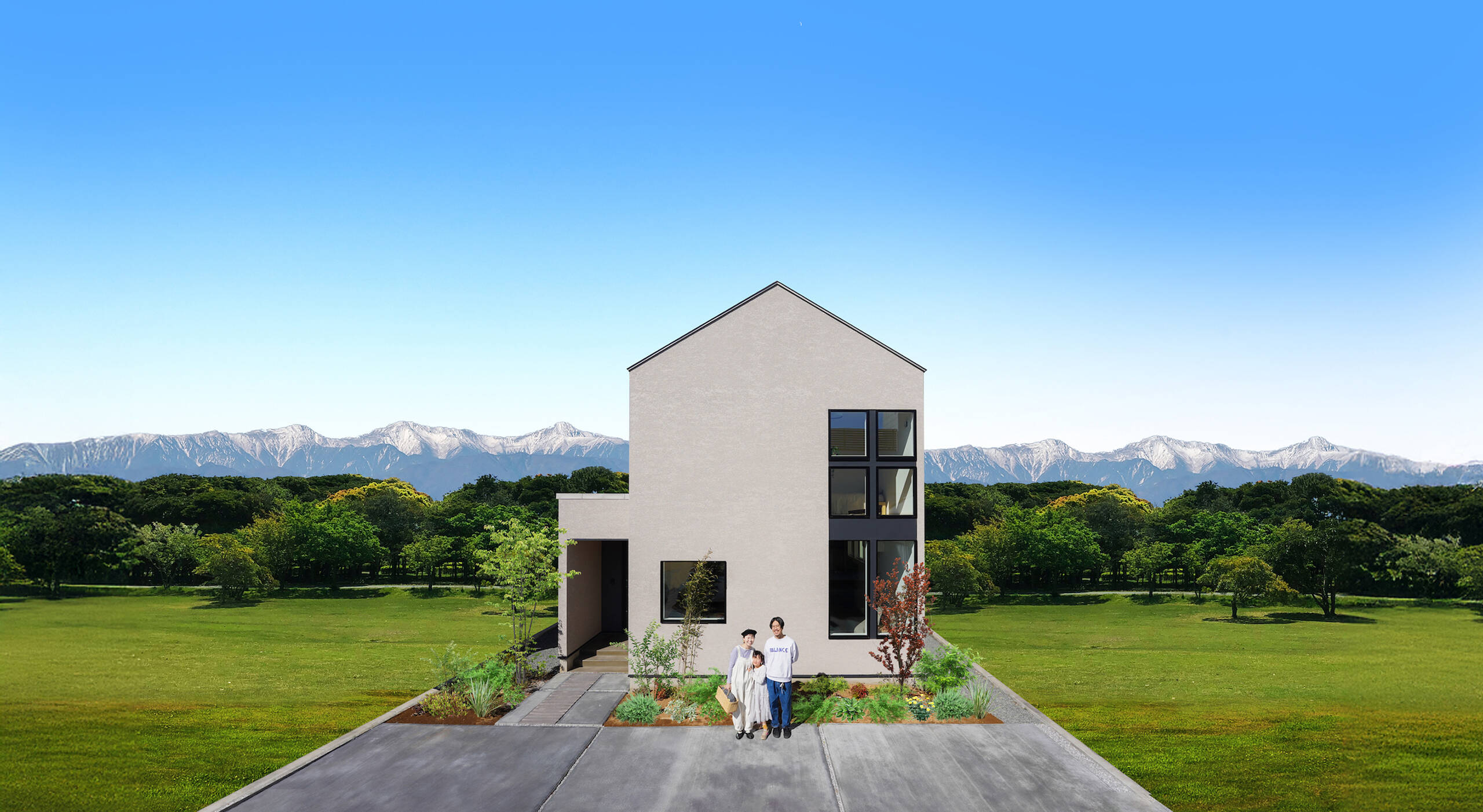 雄大な自然を背景に、モダンな家の前に立つ家族。